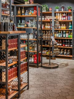 Detailaufnahme eines Spirituosen-Geschäfts mit Stahl- und Holzregalen im Industrial Design, gefüllt mit einer Vielzahl von edlen Getränkeflaschen auf einem Steinboden.